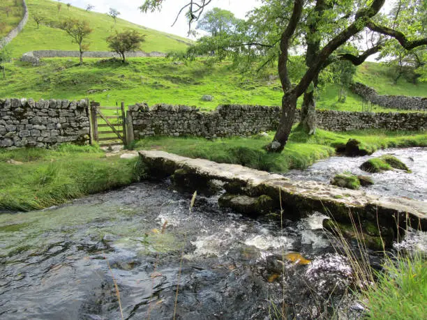 Stone clapper bridge over stream on the Pennine Way walking trail. National Trail. On path from Malham Cove cliffs to Malham. National Park. Malham, Yorkshire Dales, United Kingdom, September 5, 2019
