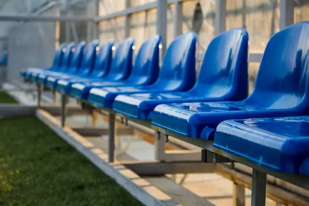 Blue plastic chairs in line for reserve players in sports stadium