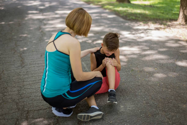 Boy with knee injury Woman looking at the boy holding his knee in pain sad teenager boy crying outdoors in park stock pictures, royalty-free photos & images