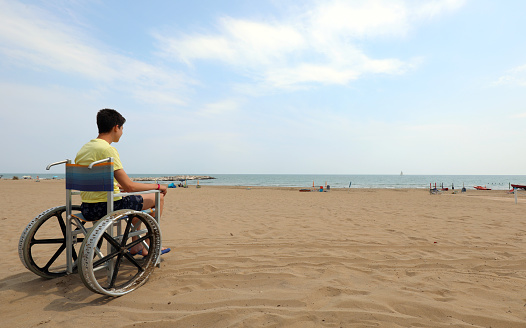 A lonely Business woman on a wheelchair looks forward to the sea against the sunset sky