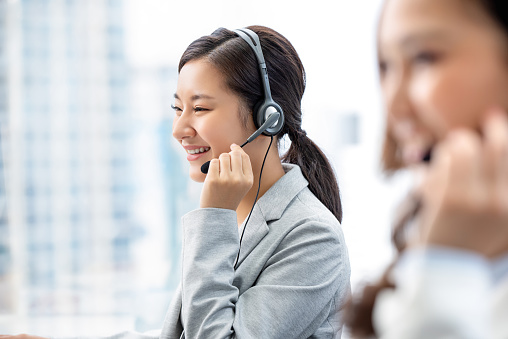 Smiling beautiful Asian woman working in call center city office as a customer service operator with team