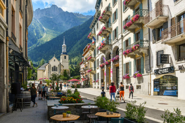 Street view with tourists, the church of Saint-Michel and Le Brévent mountain peak in the background in summer, Chamonix, Alps, France Chamonix, Haute Savoie / France - July 10 2019: Glimpse of the historic centre of the Alpine town with the church of Saint-Michel, sidewalk café and tourists in summer chamonix photos stock pictures, royalty-free photos & images