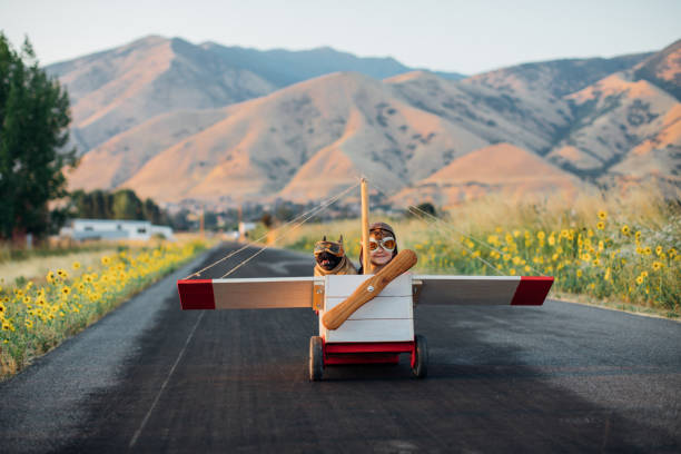 A young boy with vintage aviator goggles and a flight cap is ready for take off in his toy airplane with his pet and best friend French Bulldog riding along.  They love soaring to new heights and daydreaming of travel to new destinations.  Image taken in Utah, USA.