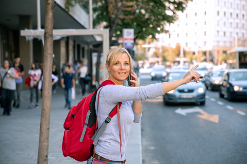 Young woman stopping taxi standing in city street waving to a car,talking on mobile phone.