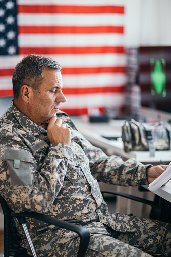 One senior soldier in uniform working on computer and reading documents.