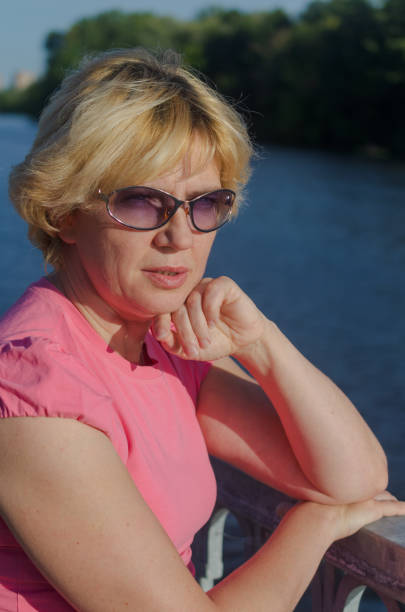 a woman of 45-50 years old sits with sadness near the river on the embankment street. - 45 50 years portrait mature women one mature woman only imagens e fotografias de stock