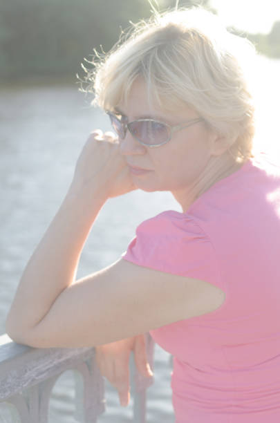 a woman of 45-50 years old sits with sadness near the river on the embankment street. - 45 50 years portrait mature women one mature woman only imagens e fotografias de stock