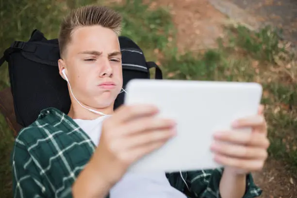 Young nervous teenager using digital tablet outdoors and watching a sports match.