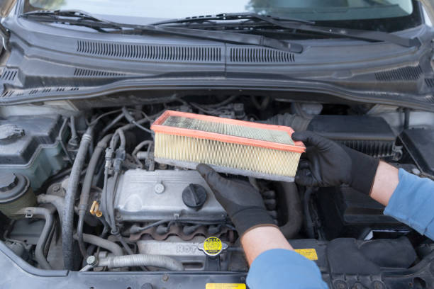 auto mechanic wearing protective work gloves holding used air filter above a car engine - air filter car motor vehicle engine imagens e fotografias de stock