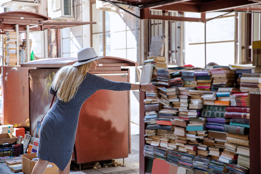 Young woman in open book store on the city street.Blonde European woman looking old books in street library