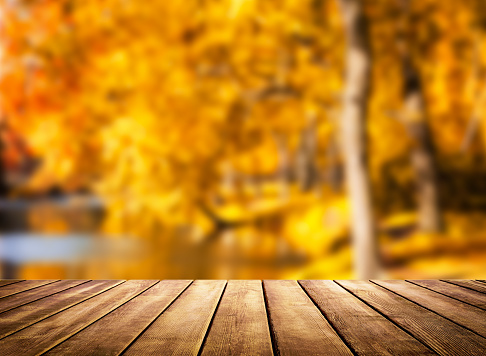 Wooden table top on blur autumn background. Autumn golden abstract background with bokeh light.