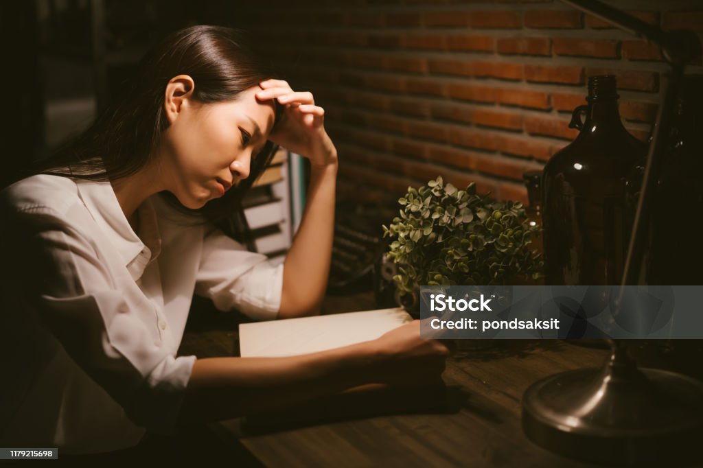 Young Asian girl stressed by the study reading in the night Writing - Activity Stock Photo