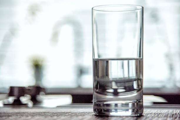 Half Full Glass of Water A drinking glass half full of water atop a modern kitchen counter top inside a home as a concept for either optimism (glass half full) or pessimism (glass half empty). pessimism photos stock pictures, royalty-free photos & images