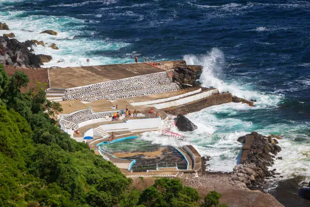 Unidentified people by a seawater swimming pool Foz da Ribeira do Guilherme seen from  Boca da Ribeira viewpoint in north east part of Sao Miguel island, Azores, Portugal. Scenic view and enjoyable summer bright day