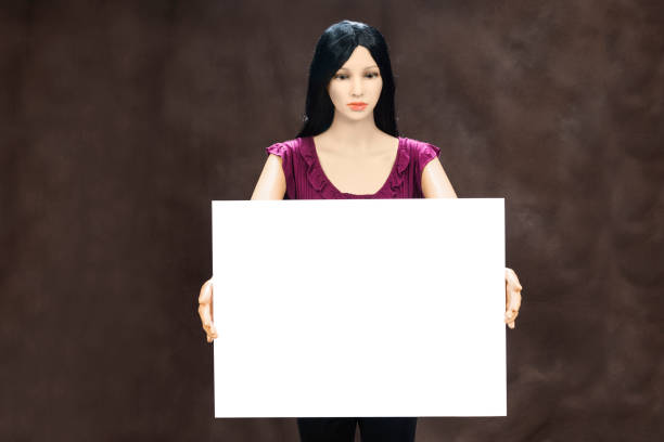 Horizontal shot of a female mannequin holding a blank white sign.  She has  long black hair and is wearing a purple blouse. Brown background. Copy space for your message.