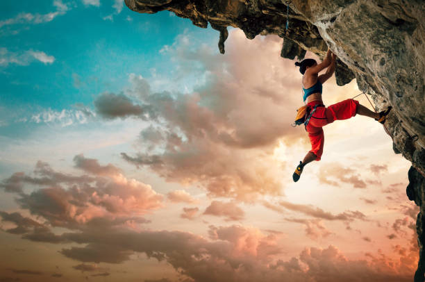 donna atletica che si arrampica su roccia rocciosa strapiombante con sfondo cielo al tramonto - scalata foto e immagini stock