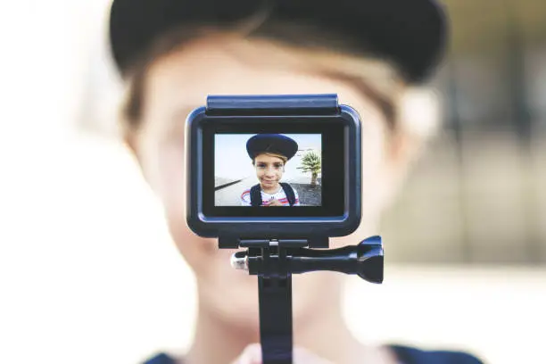 Closeup view of a teen with hat taking selfie with action cam Young blogger making video for social story with GoPro camera Student having fun with new multimedia technology device Trends tech concept