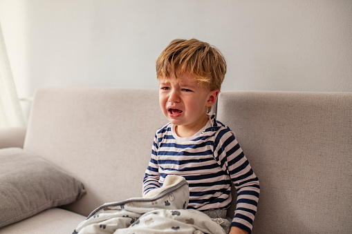 No! Little African baby boy crying while seating on the couch at home. Portrait of crying baby boy. Baby's crying one year old, brunette with brown eyes, hysteria, the crisis of the first year of life.