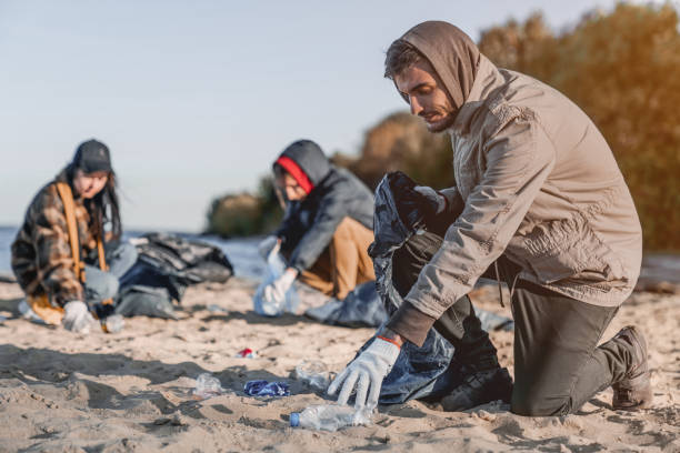 istock Handsome young volunteer with team gathering garbage on seashore 1179252586