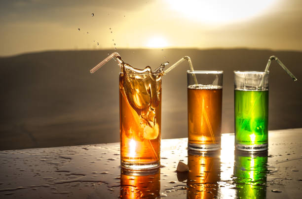 Cooling summer drink concept. Cocktail glasses splashing on sunset. Close up wet glass of cold drink on the terrace.