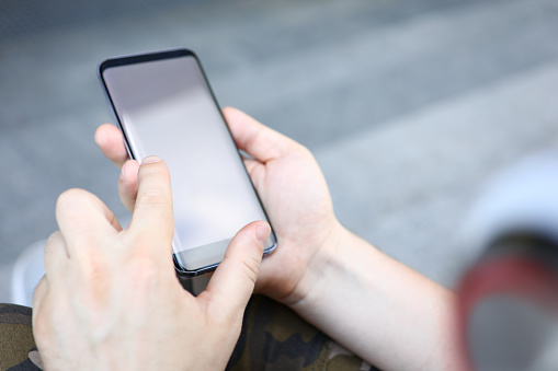 Focus on male hands holding smartphone. Man surfing internet or typing something on cellphone. Latest technology concept. Copy space on screen. Blurred background