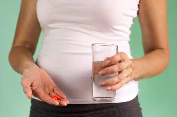 una chica embarazada sostiene un vaso de agua y pastillas en sus manos. mantener la salud de la madre y el bebé. - twin tips fotografías e imágenes de stock