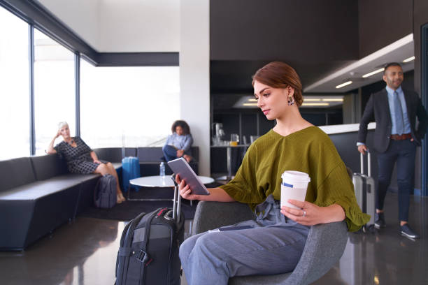 millennial female traveller with coffee sitting in modern airport terminal streaming video on tablet - mobility working digital tablet people imagens e fotografias de stock