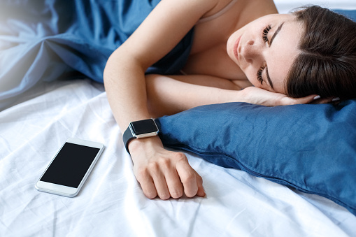 Young woman lying on bed bedtime sleeping smartphone and digital watch close-up