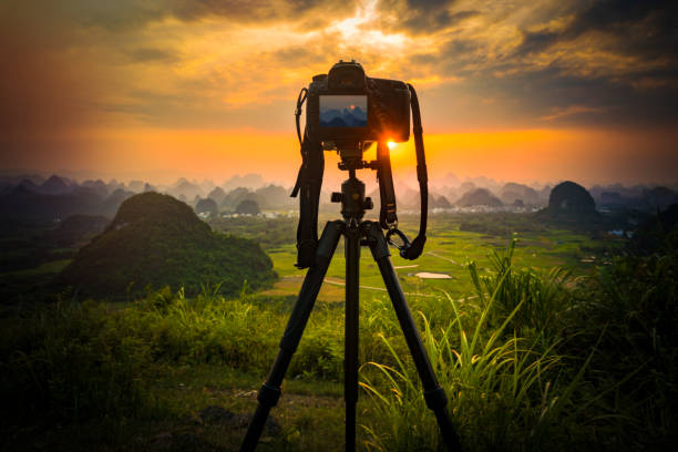 fotocamera su treppiede e fotocamera vista fotografia con sfocato paesaggio di messa a fuoco dell'alba al tramonto sole nuvola di cielo chiaro - treppiede foto e immagini stock