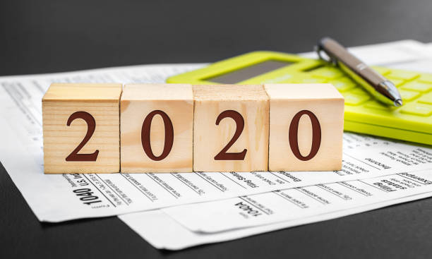 2020年繳稅。木立方體的數位為2020年，稅表和計算機的黑色。 - 1040 稅表 圖片 個照片及圖片檔