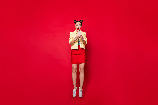 Full body photo of pretty jumping, lady holding telephone hands wear casual outfit isolated red background