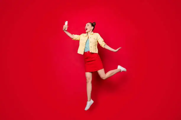Photo of Pretty jumping lady holding telephone hands making selfies in air wear casual outfit isolated red background