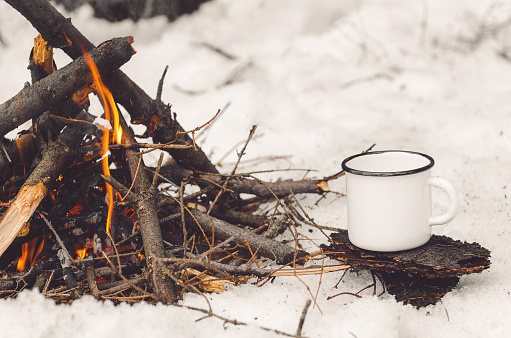 Walking mug with coffee near the campfire. Concept hike, walk, trip in winter.