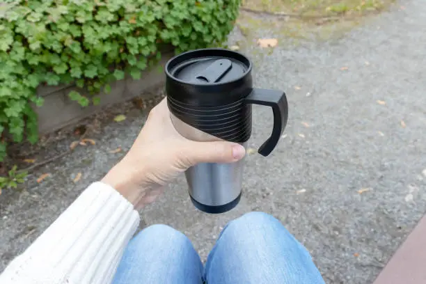 Woman holding a metal thermo cup with hot drink, tea or coffee.