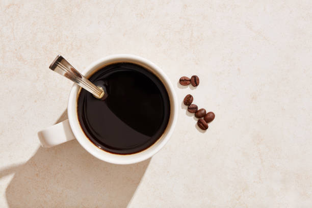 Dark black coffee in a white mug with coffee beans under harsh summer sunlight Dark black coffee in a white mug with coffee beans under harsh summer sunlight. Overhead view. black coffee from above stock pictures, royalty-free photos & images