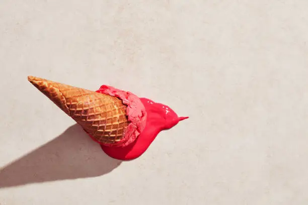 Photo of Strawberry ice cream with waffle cone dropped on the floor and melting on the ground under hot summer light