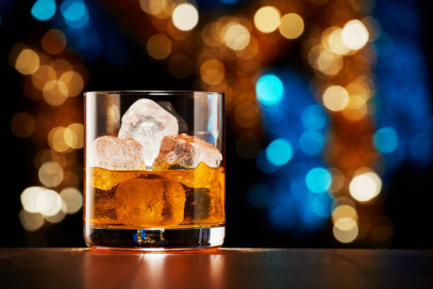 Glass of whiskey with ice on colorful Christmas lights bokeh background Glass of whiskey with ice on colorful Christmas lights bokeh background whiskey photos stock pictures, royalty-free photos & images