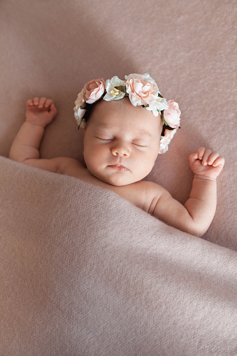 Portrait of cute newborn baby girl wearing flower headband and sleeping under pink blanket. Vertical Image with copy space. Innocence concept.