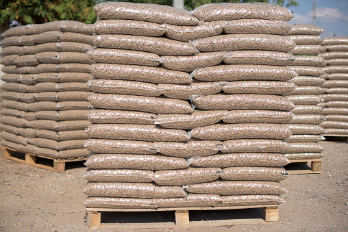 Piles of plastik bags full with wooden pellets arranged in rows and columns on pallets