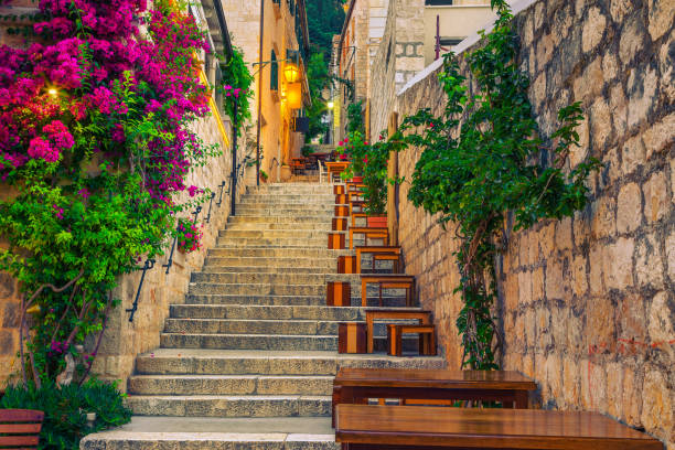 Narrow street and street cafe decorated with flowers, Hvar, Croatia Cozy narrow street with street cafe and restaurant at morning. Rustic street with stone houses and colorful bougainvillea mediterranean flowers, Hvar town, Hvar island, Dalmatia, Croatia, Europe hvar photos stock pictures, royalty-free photos & images