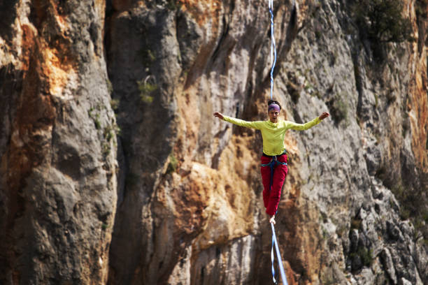 a woman is walking along a stretched sling. highline in the mountains. woman catches balance. performance of a tightrope walker in nature. - new york canyon imagens e fotografias de stock