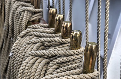 Light grey marine ropes around brass handles on board of a luxury threemaster sailing yacht