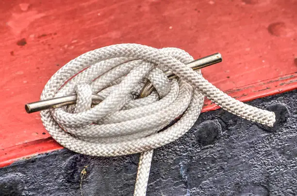 White marine rope tied in a nautical knot on the red and black steel hull of a sailing yacht