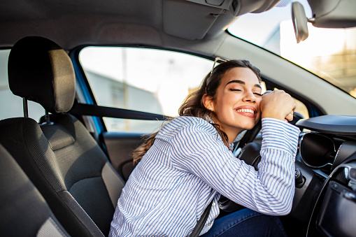 Mujer joven y alegre disfrutando de nuevo coche abrazando volante sentado en el interior photo