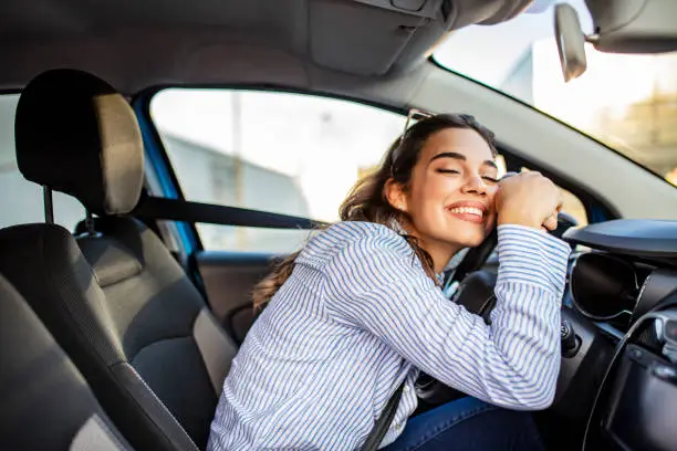 Photo of Young and cheerful woman enjoying new car hugging steering wheel sitting inside