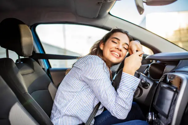 Young and cheerful woman enjoying new car hugging steering wheel sitting inside. Woman driving a new car. Woman Driver Portrait at Car