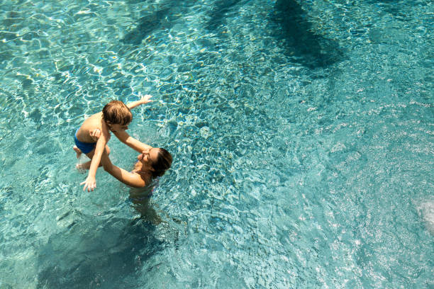 Above view of happy single mother and her son having fun in the pool. High angle view of happy mother having fun with her small son in the swimming pool. Copy space. swimming pool stock pictures, royalty-free photos & images