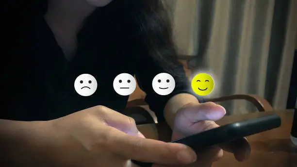 Photo of Customer experience concept. A woman using smartphone choose happy smile face icon. Depicts that customer is very satisfied.