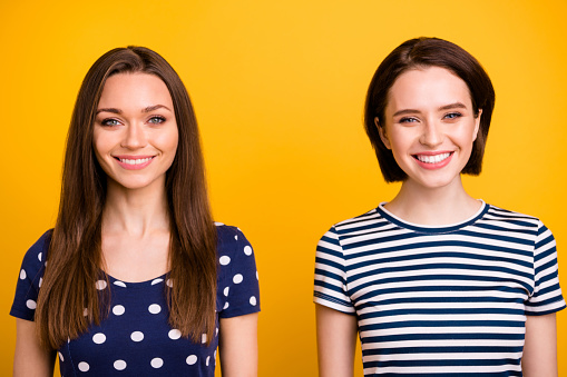 Close up photo of two amazing positive ladies with lovely beaming smile in good mood, wear summer casual t-shirts isolated yellow background