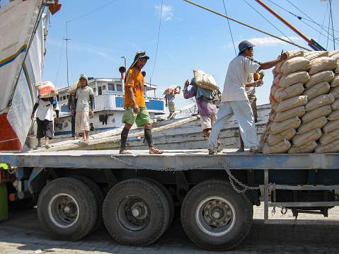 Jakarta, Indonesia - July 13, 2009: unskilled workers loading sacks with cement from a truck onto a wooden transport vessel